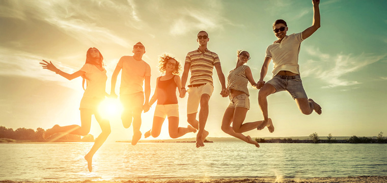 Sechs junge Menschen springen am Strand ausgelassen in die Luft.